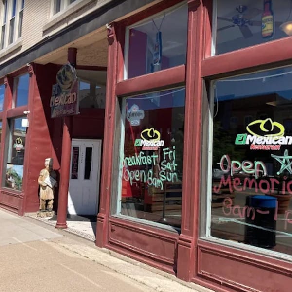 Exterior of El Mexican Restaurant with red facade, large windows displaying opening hours, and a statue.