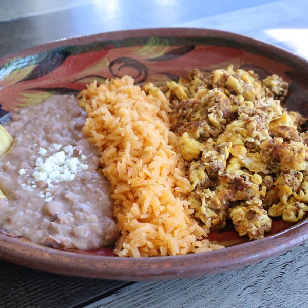A colorful plate of Mexican food with refried beans, rice, and scrambled eggs with chorizo.