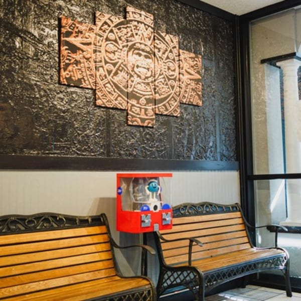 Waiting area with two wooden benches, a red gumball machine, and a large Mayan calendar art piece.