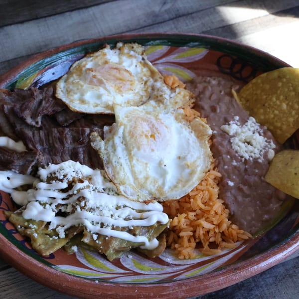 A Mexican breakfast plate with steak, two fried eggs, chilaquiles, rice, refried beans, and tortilla chips.