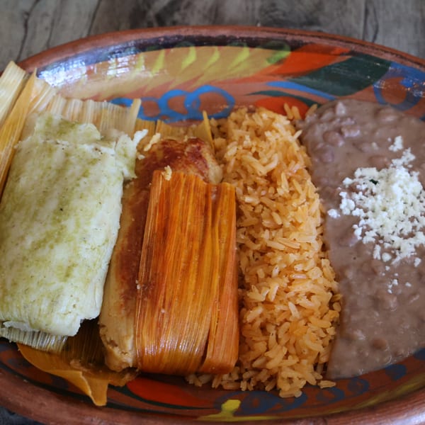 A colorful plate of Mexican tamales, rice, and refried beans with crumbled cheese.