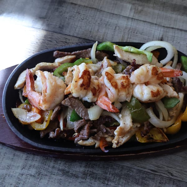 Sizzling Mexican fajitas with shrimp, chicken, beef, onions, and bell peppers on a cast iron platter.
