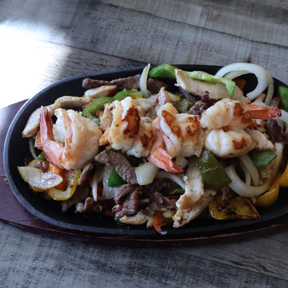 Sizzling Mexican fajitas with shrimp, chicken, beef, onions, and bell peppers on a cast iron platter.