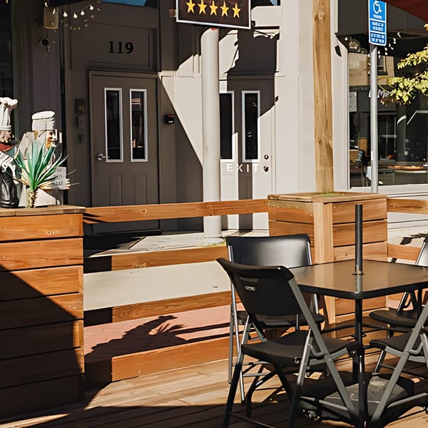 Outdoor patio seating area with wooden railings, black tables, and chairs in front of El Mexican Restaurant.
