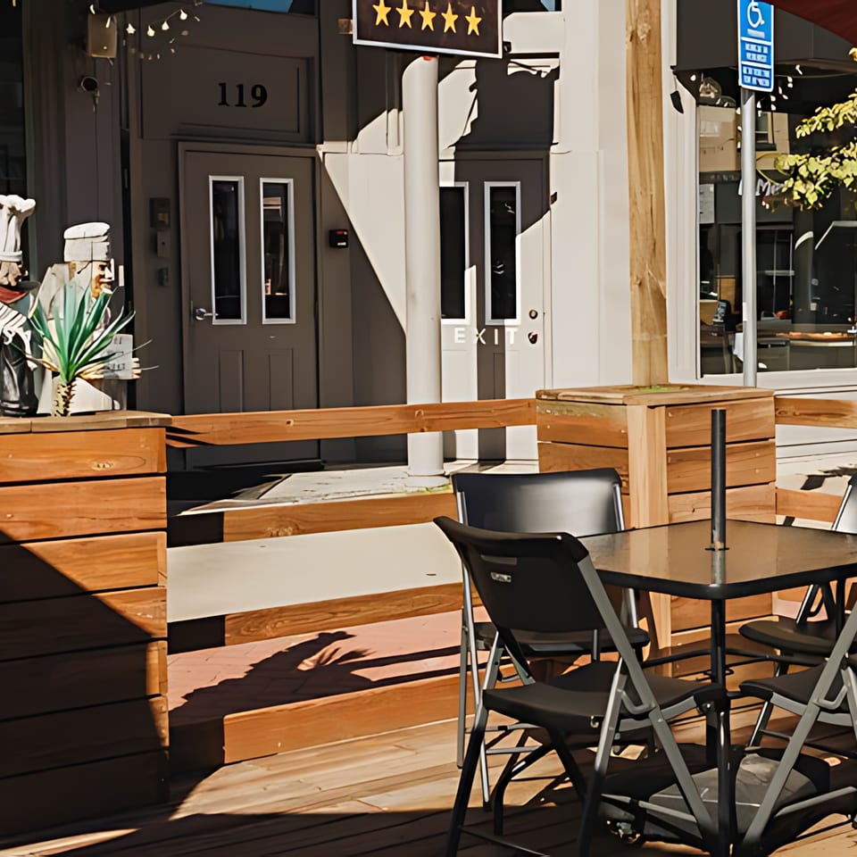 Outdoor patio seating area with wooden railings, black tables, and chairs in front of El Mexican Restaurant.